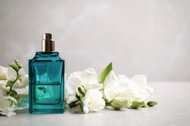 Photo of Bottle of perfume and beautiful flowers on light table. Space for text