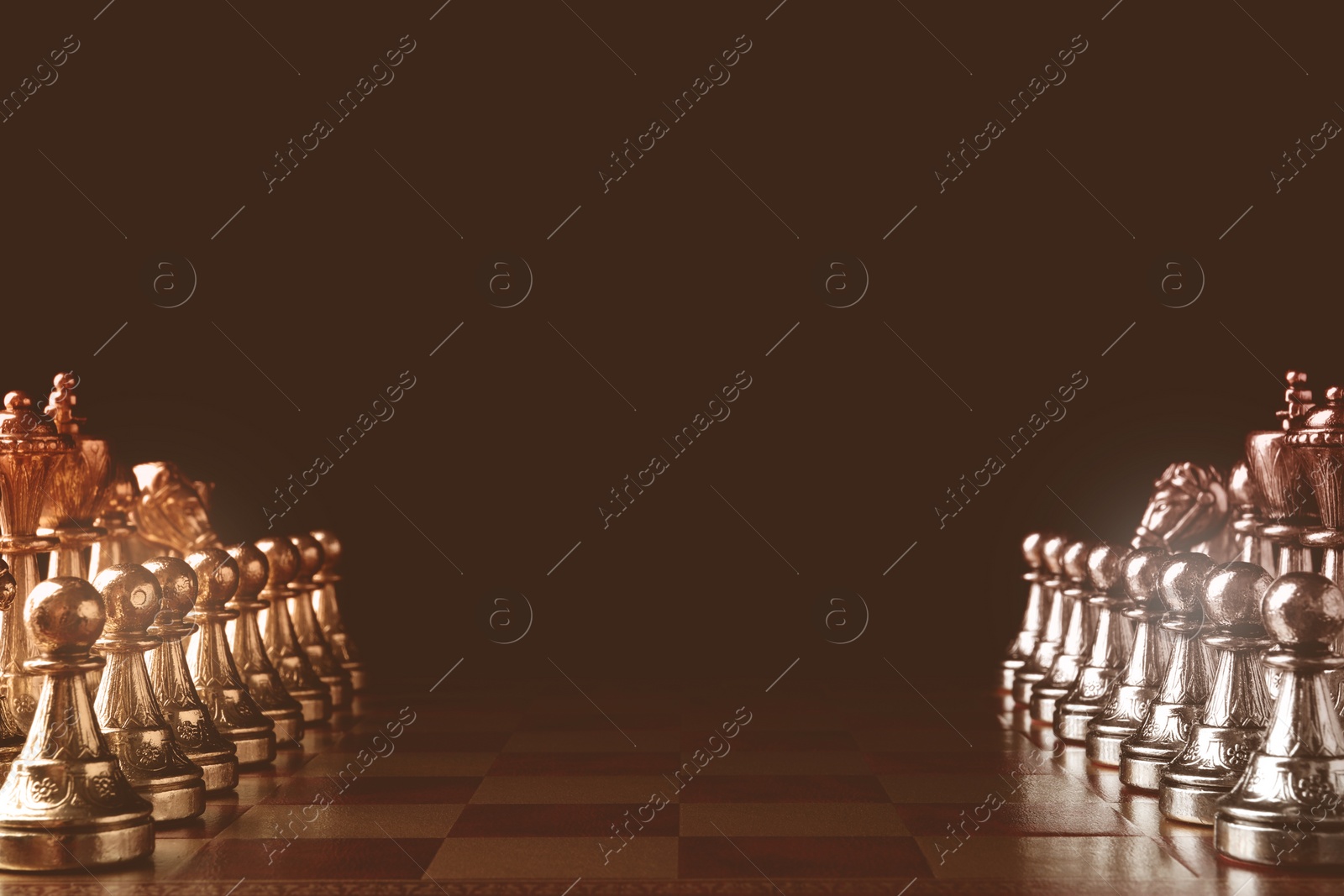 Image of Chessboard with game pieces in starting position on black background, sepia toned