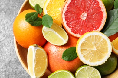 Photo of Different fresh citrus fruits and leaves in bowl on table, top view