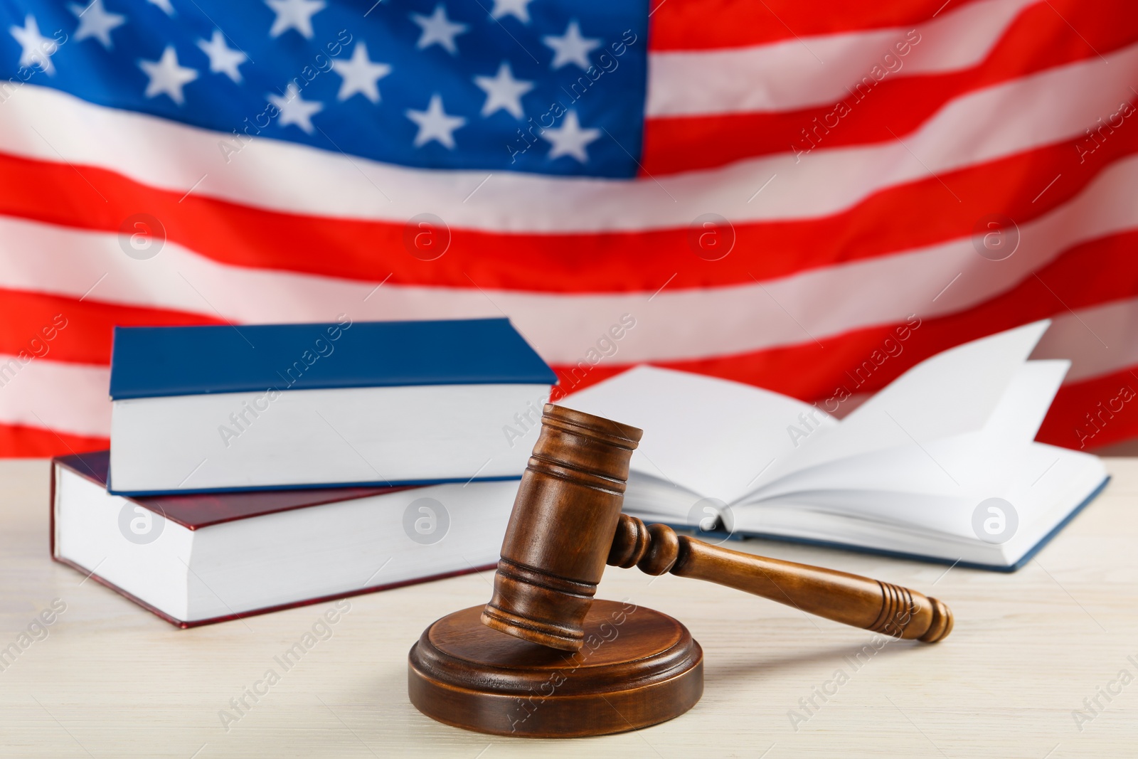 Photo of Judge's gavel and books on white wooden table against American flag