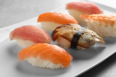Photo of Plate with delicious nigiri sushi on grey table, closeup