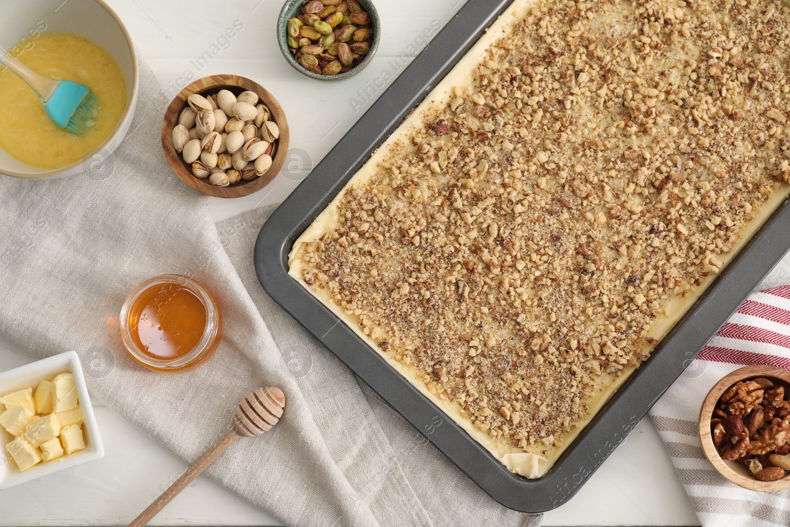 Photo of Making delicious baklava. Baking pan with dough and ingredients on white table, flat lay