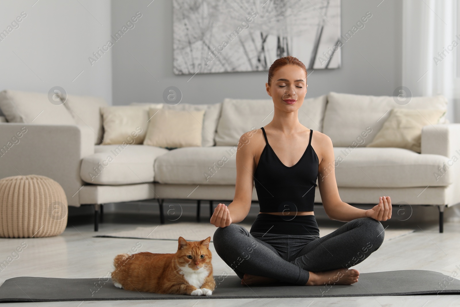 Photo of Beautiful woman with cute red cat practicing yoga on mat at home