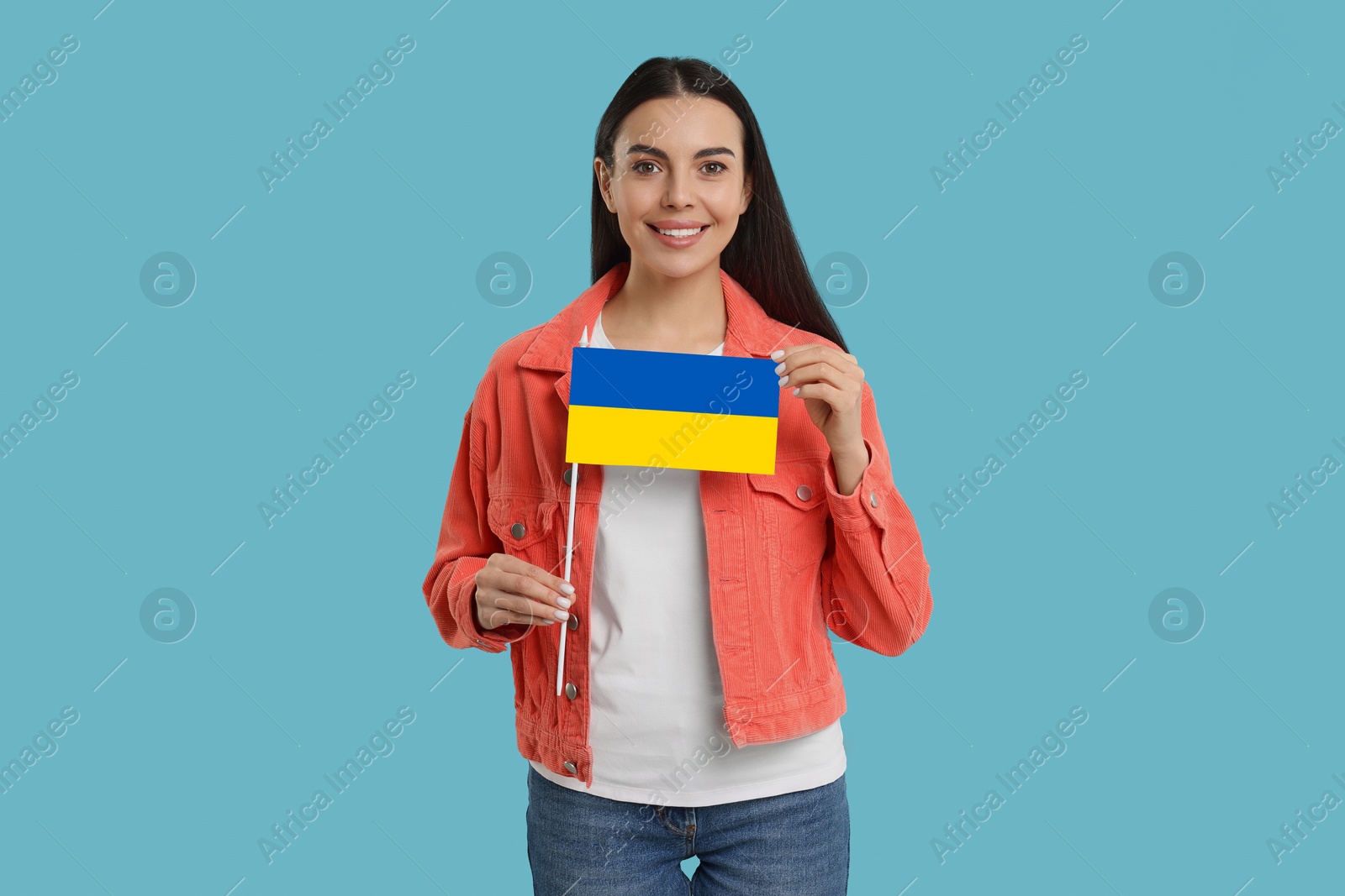 Image of Happy young woman with flag of Ukraine on light blue background