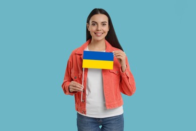 Happy young woman with flag of Ukraine on light blue background