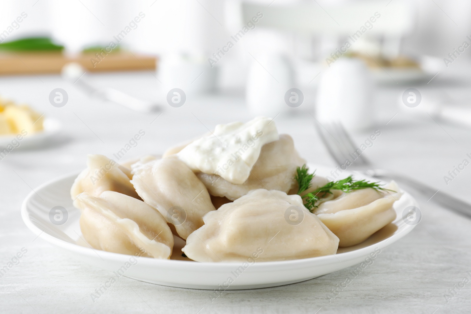 Photo of Plate of tasty dumplings served with sour cream and dill on table