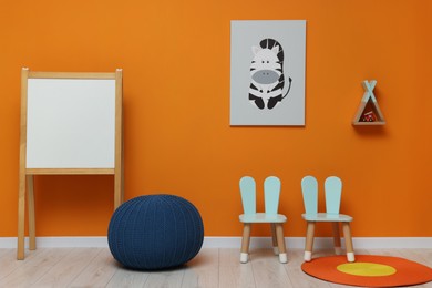 Photo of Modern furniture near orange wall in playroom. Stylish kindergarten interior
