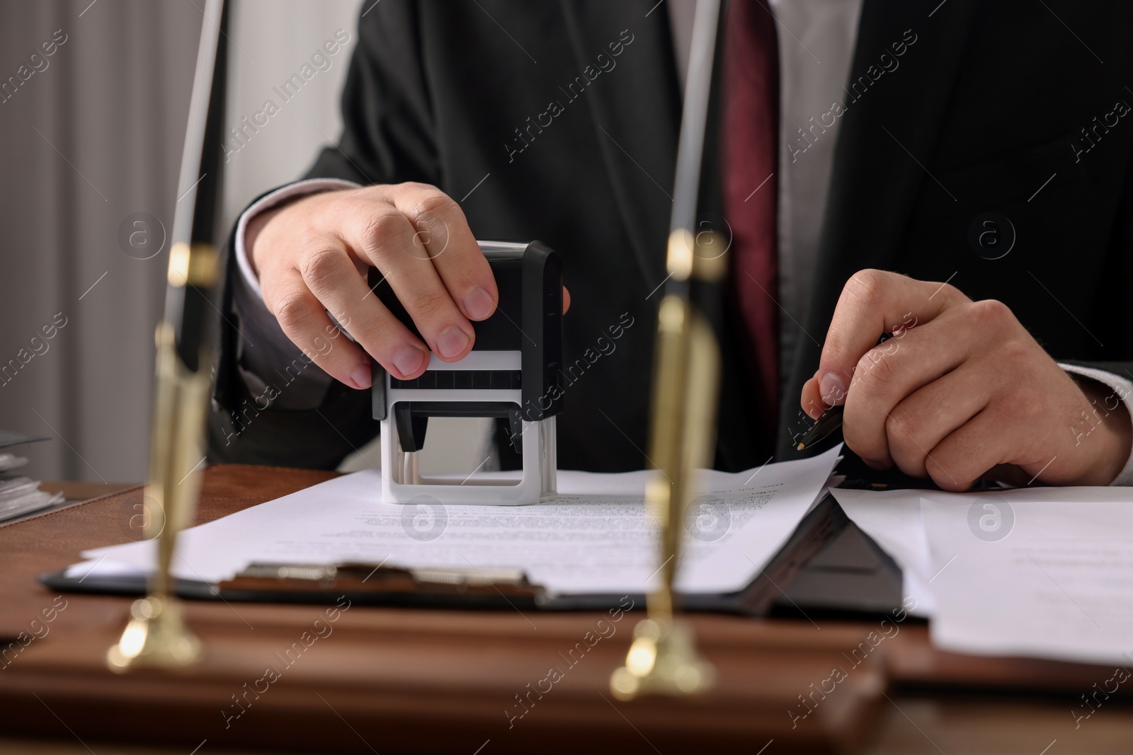 Photo of Notary with pen stamping document at table in office, closeup