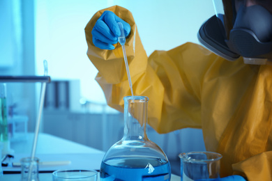 Photo of Scientist in chemical protective suit working at laboratory, closeup. Virus research