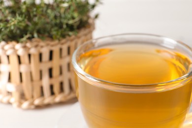 Photo of Aromatic herbal tea with thyme in glass cup on table, closeup