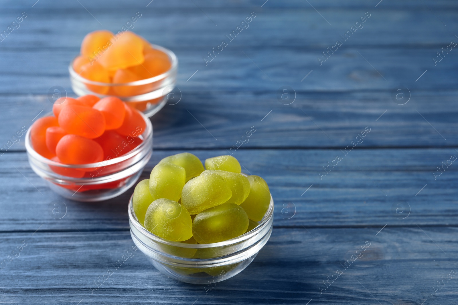 Photo of Glass bowls with tasty jelly candies on blue wooden table, space for text