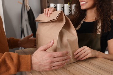 Worker giving paper bag to customer in cafe, closeup