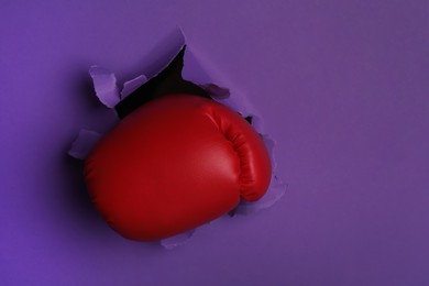 Photo of Man breaking through purple paper with boxing glove, closeup. Space for text