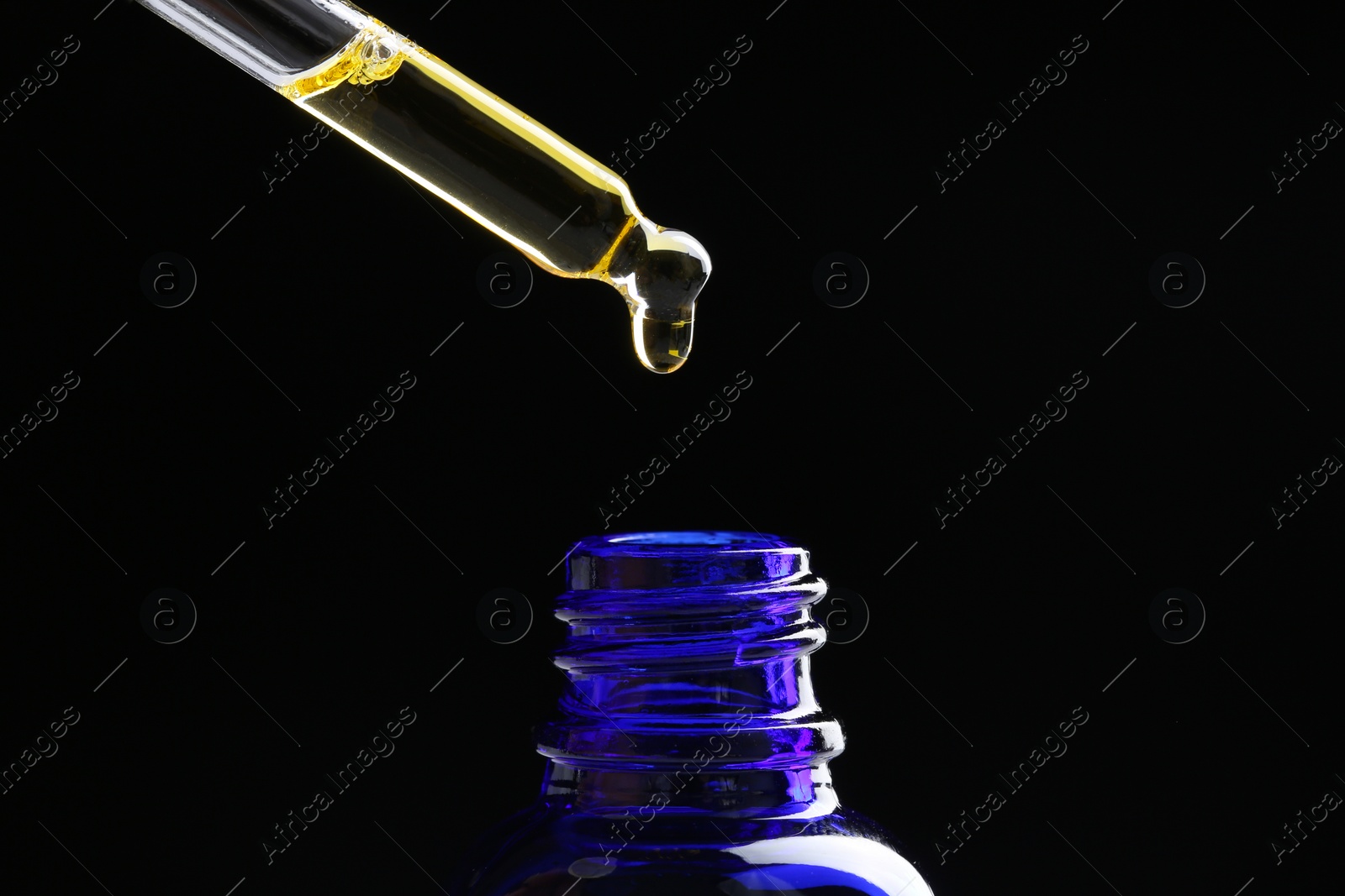 Photo of Dripping tincture from pipette into bottle on black background, closeup