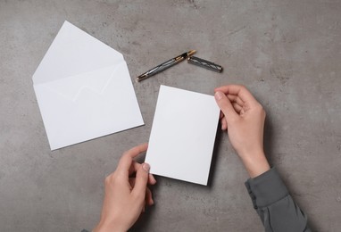 Photo of Woman with blank sheet of paper at grey textured table, top view. Space for text