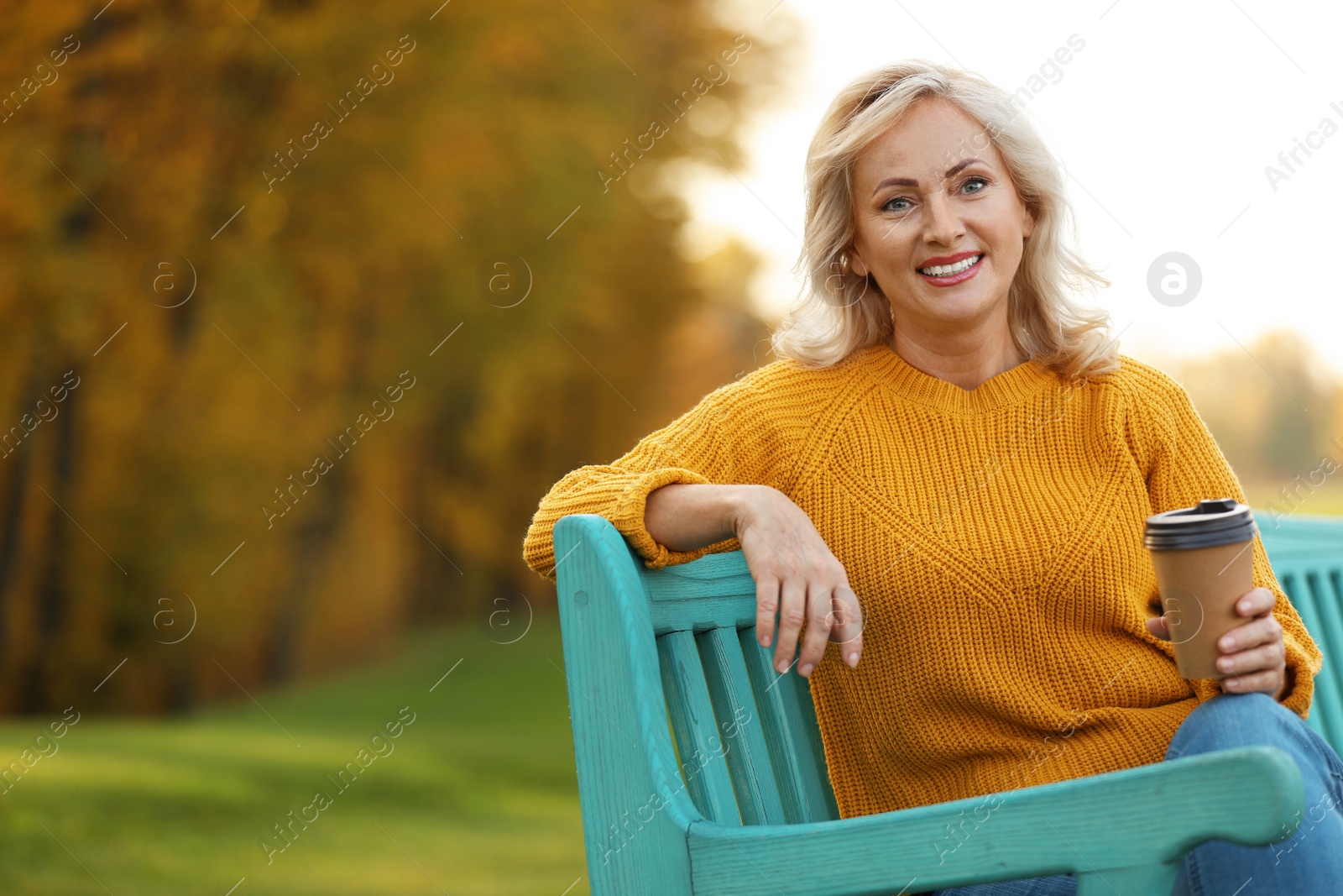 Photo of Beautiful mature woman with cup of coffee on bench in park