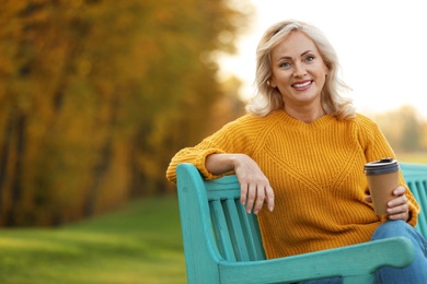 Beautiful mature woman with cup of coffee on bench in park