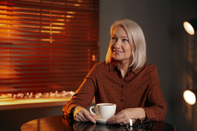 Photo of Beautiful mature woman with cup of coffee indoors. Space for text