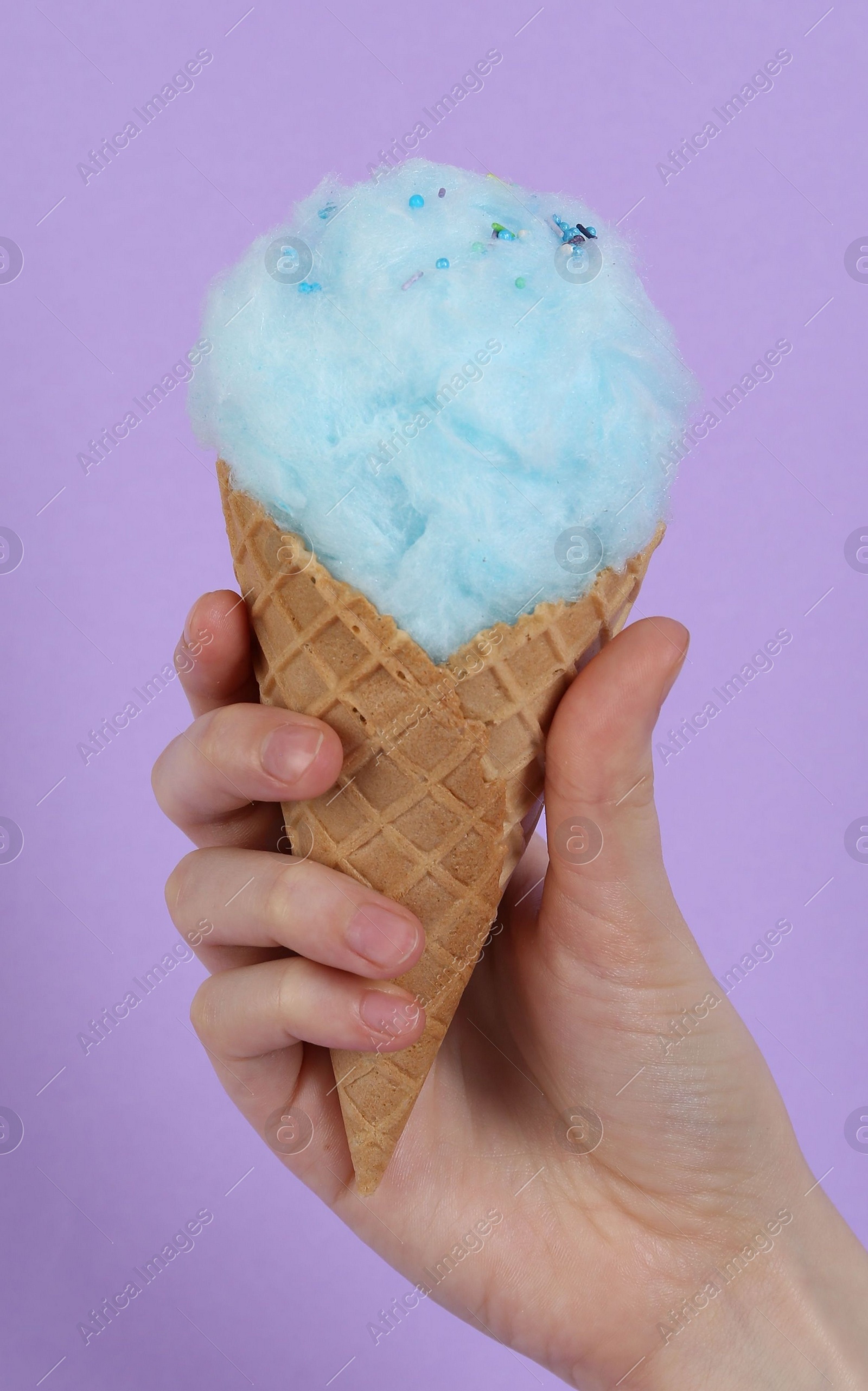 Photo of Woman holding waffle cone with cotton candy on violet background, closeup