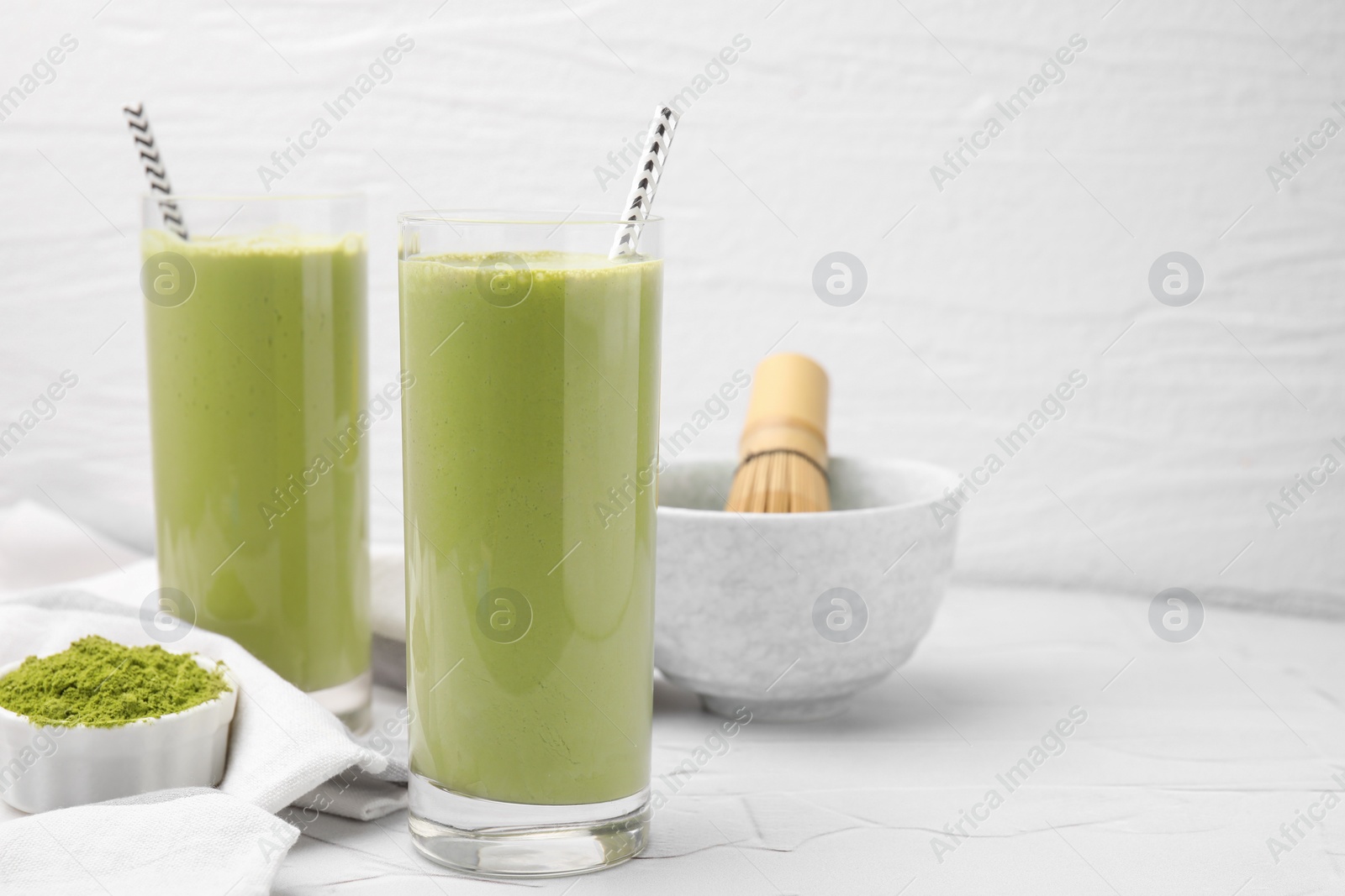 Photo of Glasses of tasty matcha smoothie and powder on white table, space for text