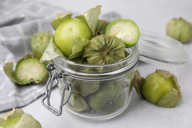 Fresh green tomatillos with husk in glass jar on light table, closeup