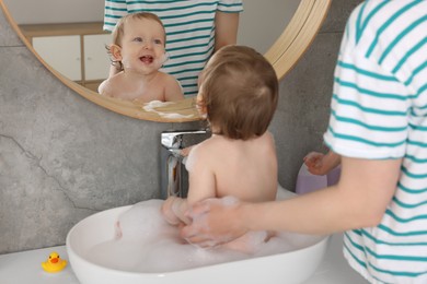 Photo of Mother washing her little baby in sink at home