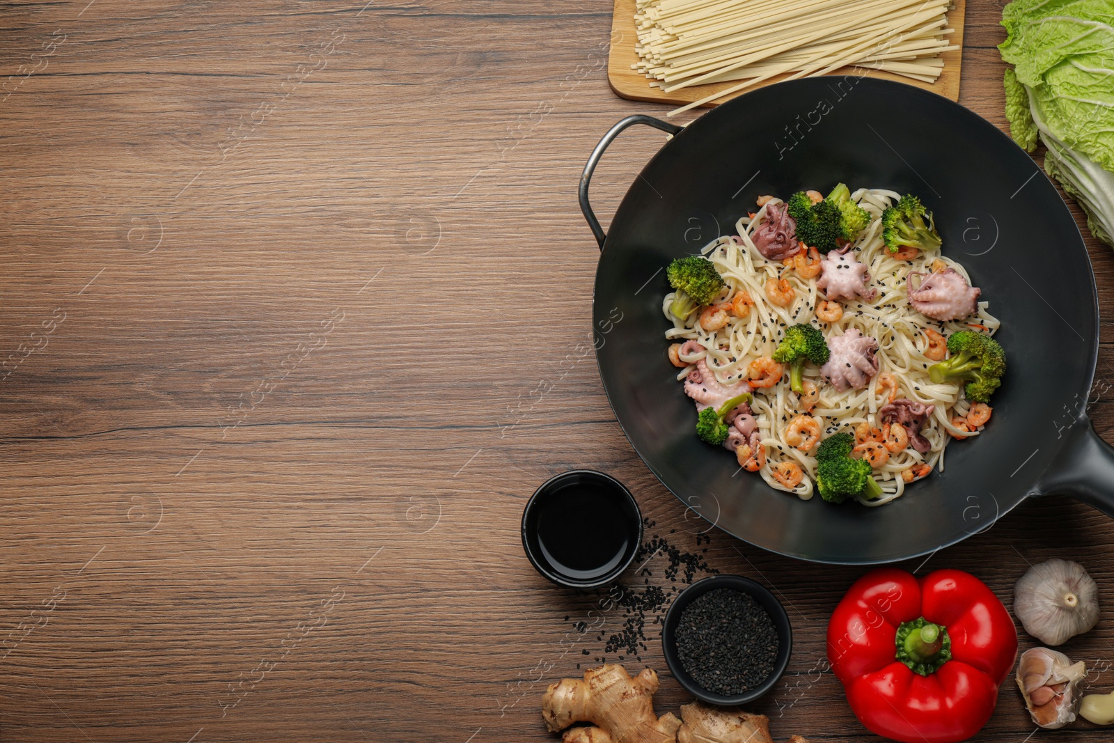 Photo of Stir fried noodles with seafood and vegetables in wok on wooden table, flat lay. Space for text