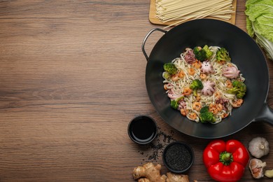 Stir fried noodles with seafood and vegetables in wok on wooden table, flat lay. Space for text