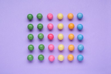 Many bright chewy gumballs on lilac background, flat lay