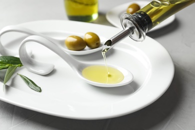 Photo of Pouring fresh olive oil into spoon on plate