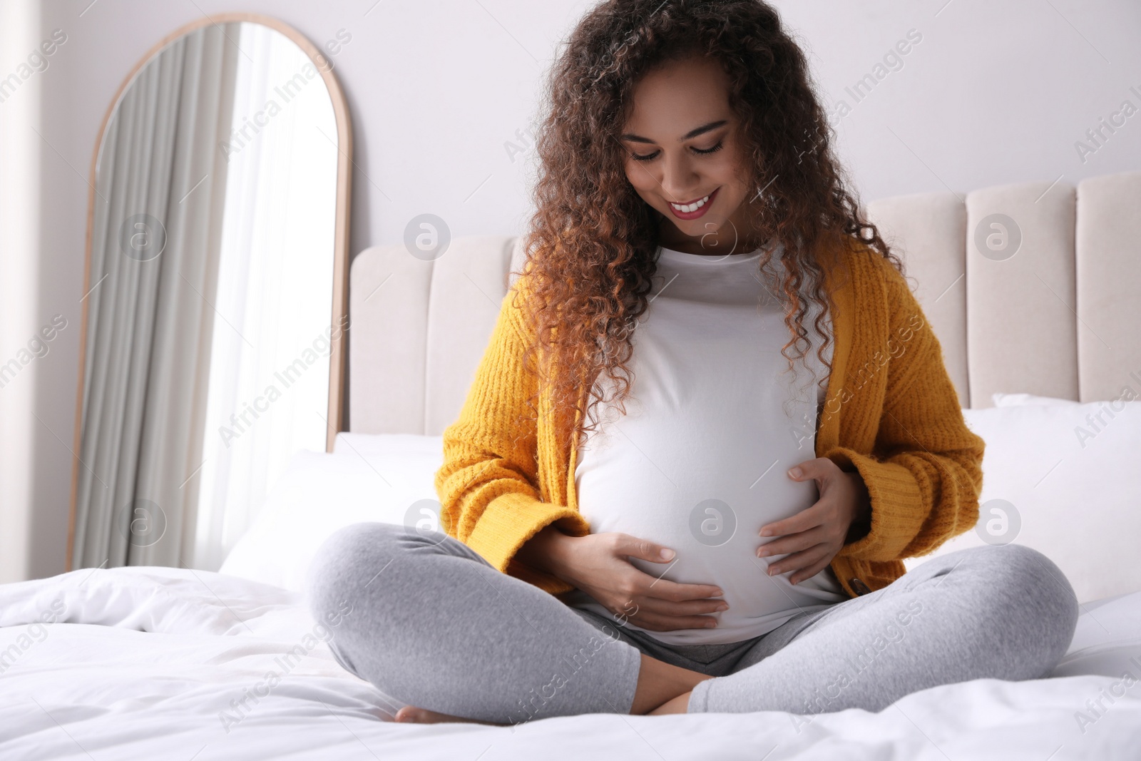 Photo of Pregnant young African-American woman sitting on bed at home