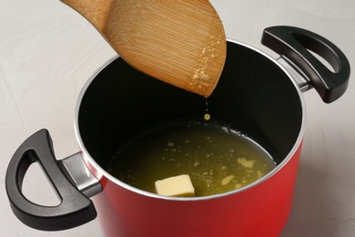 Spatula over pot with melting butter on grey table, closeup