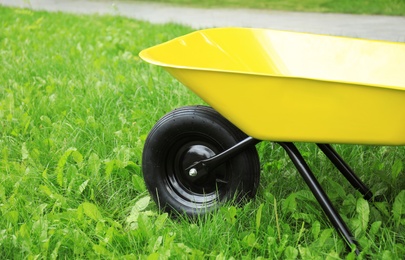 Photo of Yellow wheelbarrow on green grass outdoors. Gardening tool