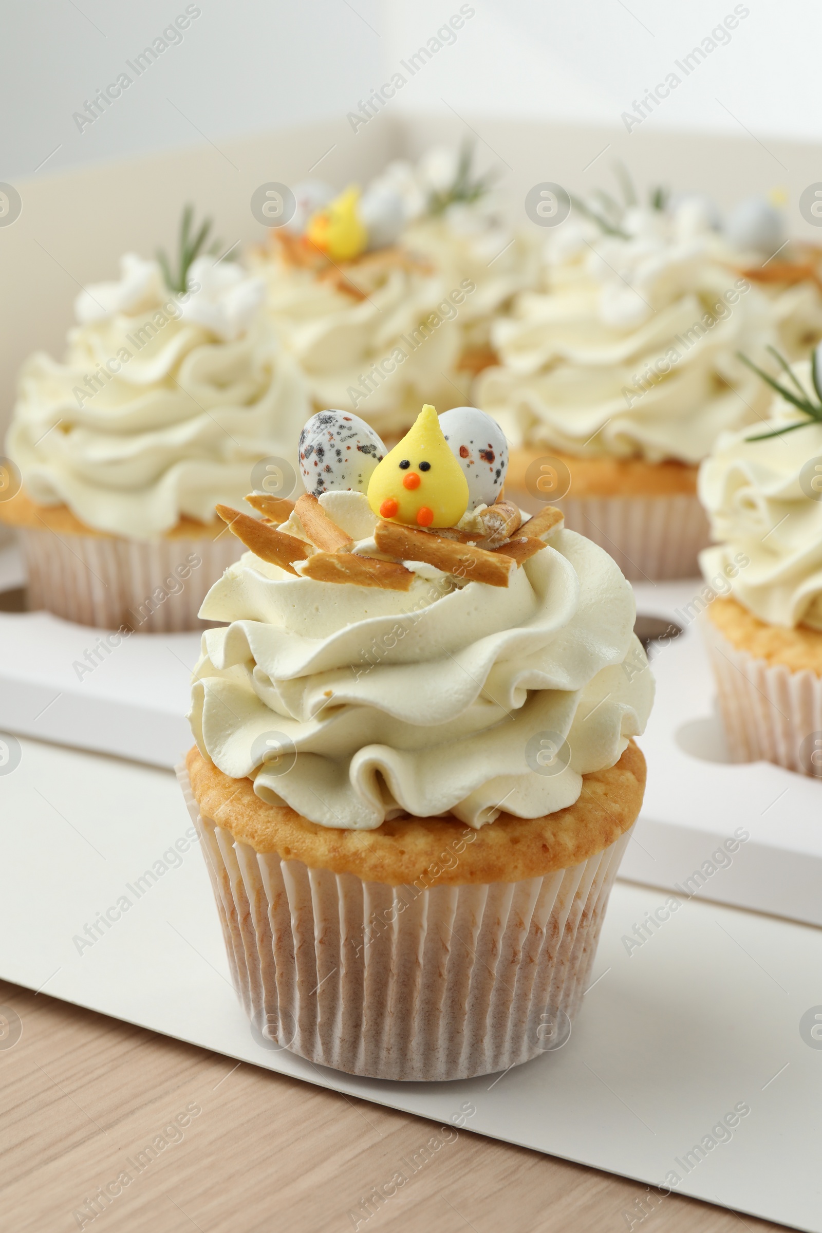 Photo of Tasty Easter cupcakes in box on wooden table, closeup