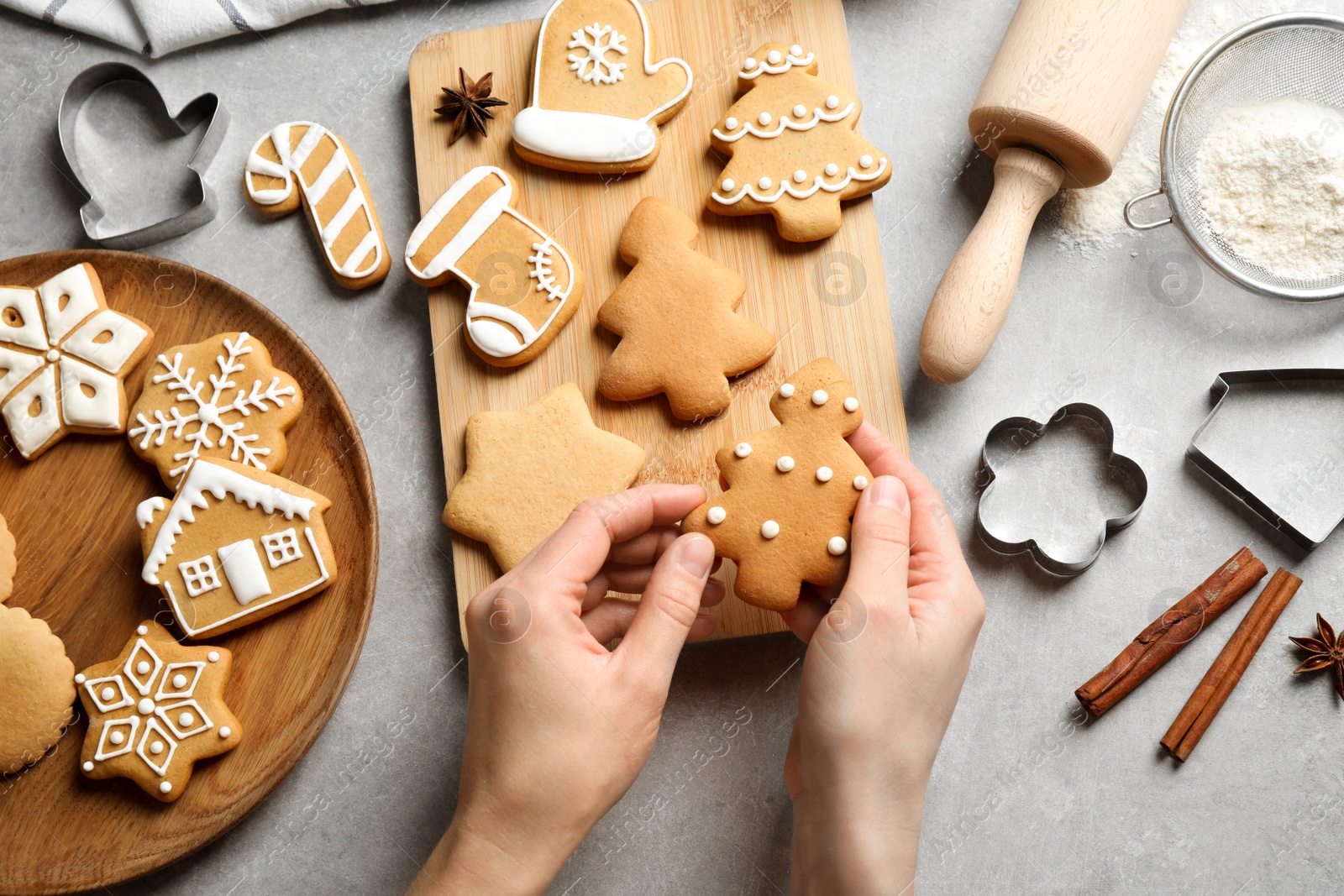 Photo of Woman holding tasty homemade Christmas cookie over grey table, top view. Closeup