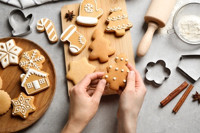 Photo of Woman holding tasty homemade Christmas cookie over grey table, top view. Closeup