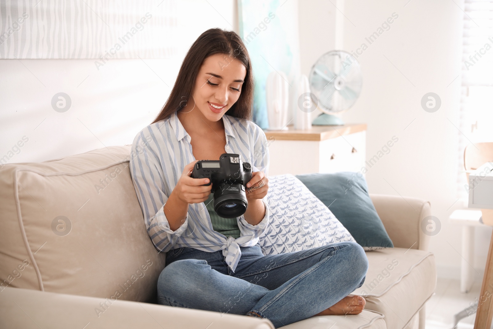 Photo of Young photographer with professional camera on sofa indoors