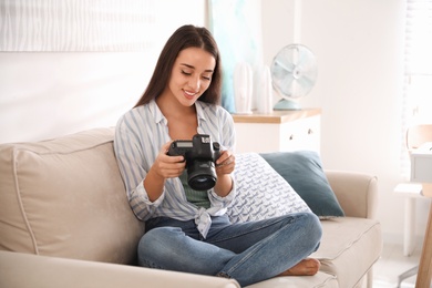 Photo of Young photographer with professional camera on sofa indoors