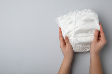 Woman with diapers on light grey background, closeup. Space for text