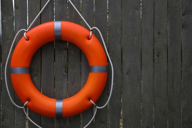 Photo of Orange lifebuoy hanging on grey wooden fence, space for text. Rescue equipment