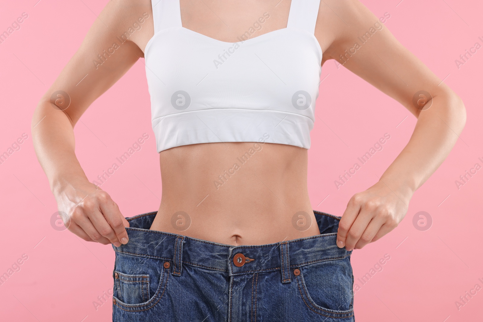 Photo of Slim woman wearing big jeans on pink background, closeup. Weight loss