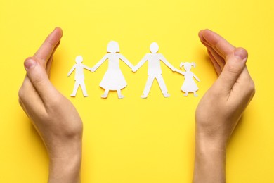 Photo of Woman protecting paper cutout of family on yellow background, top view