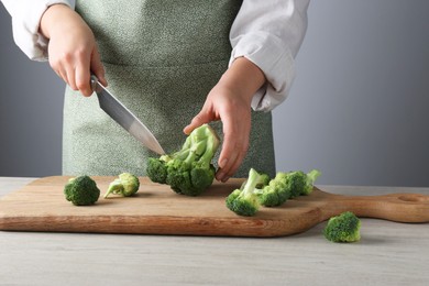 Photo of Woman cutting fresh broccoli at wooden table, closeup