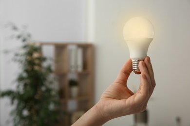 Photo of Woman holding lamp bulb on blurred background, closeup with space for text