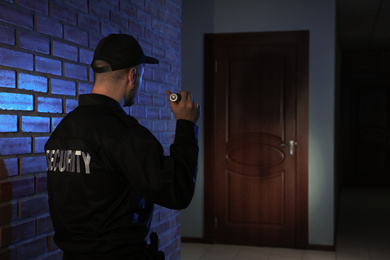 Male security guard with flashlight in dark corridor