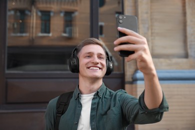 Photo of Smiling man in headphones taking selfie outdoors