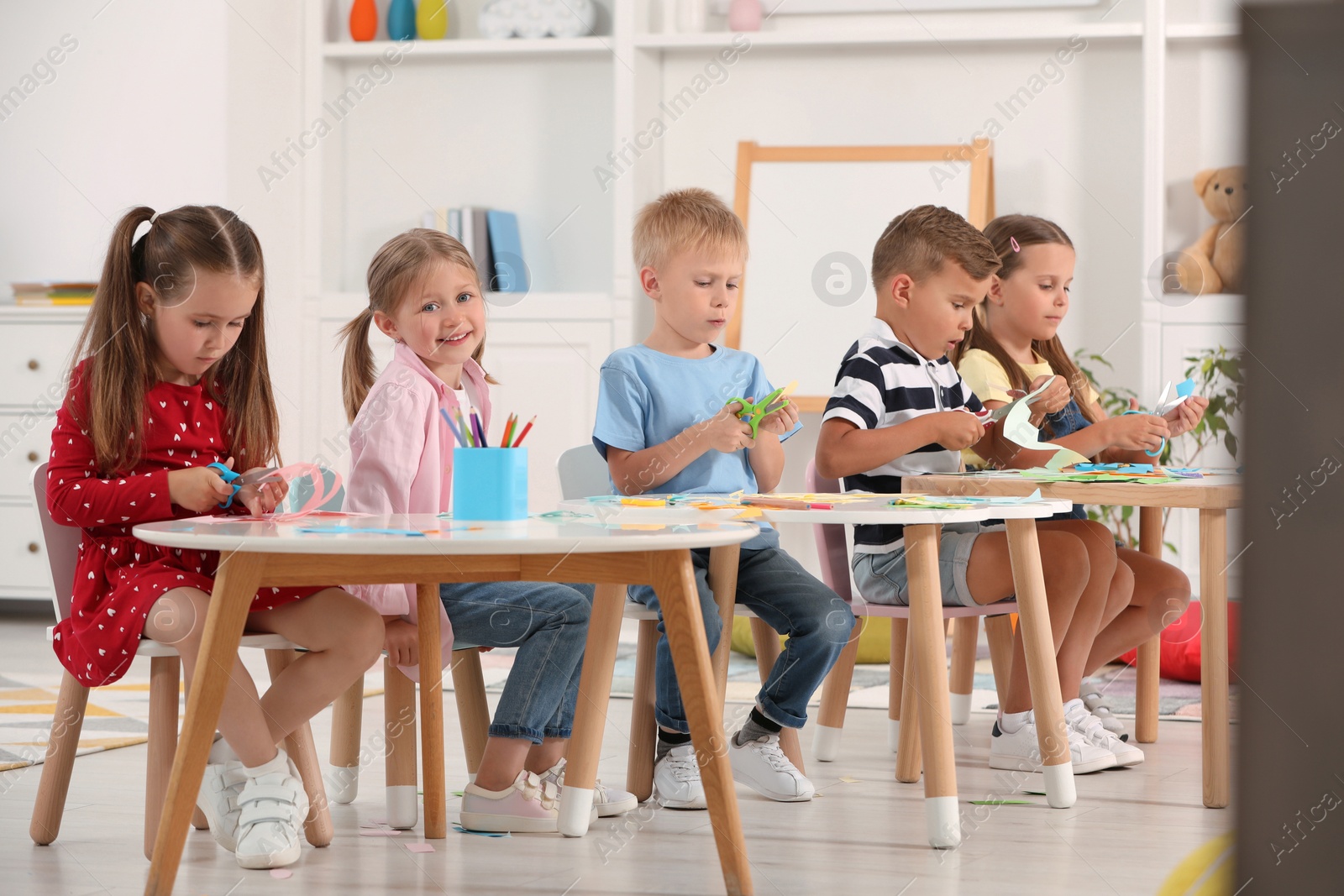 Photo of Group of cute little children making toys from color paper at desks in kindergarten. Playtime activities