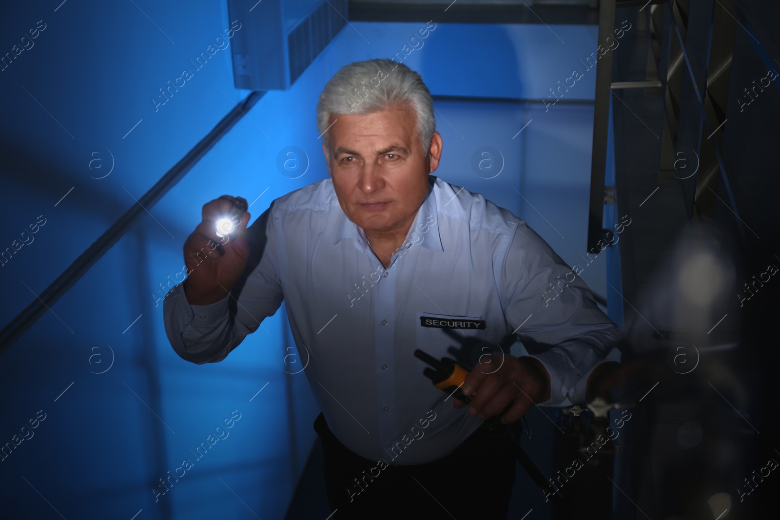 Photo of Professional security guard with flashlight on stairs in dark room