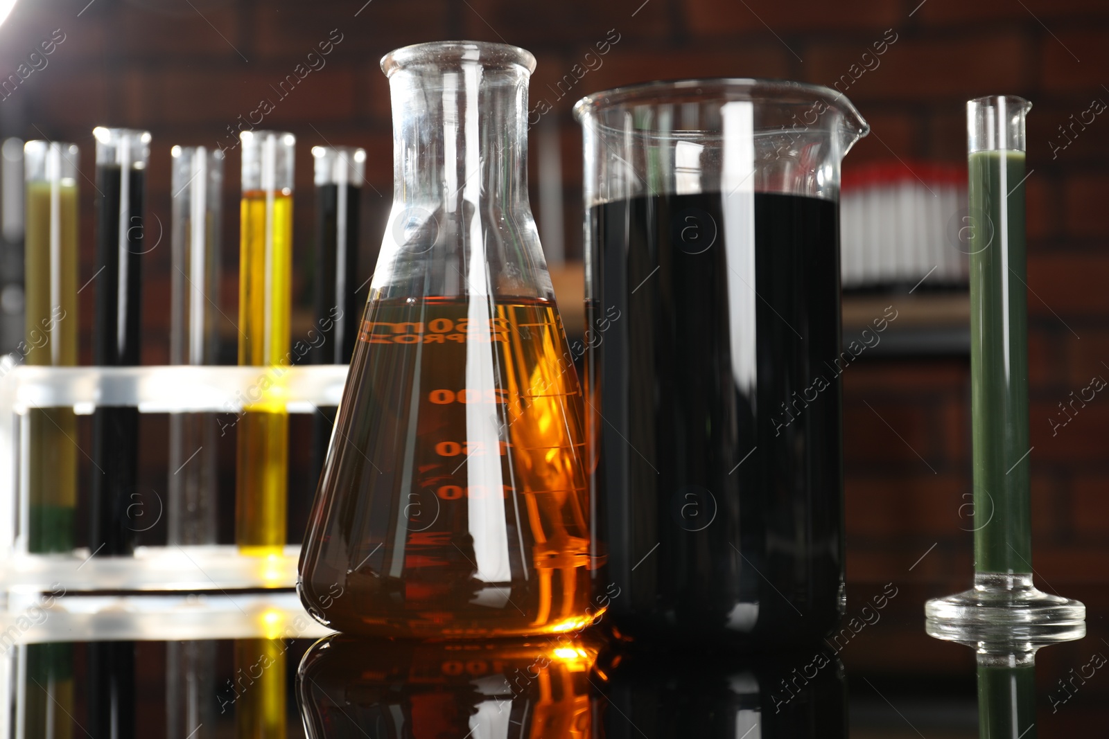 Photo of Laboratory glassware with different types of oil on black mirror table indoors, closeup
