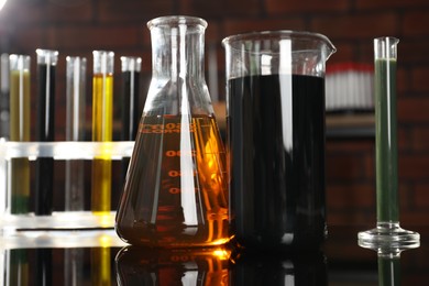 Photo of Laboratory glassware with different types of oil on black mirror table indoors, closeup